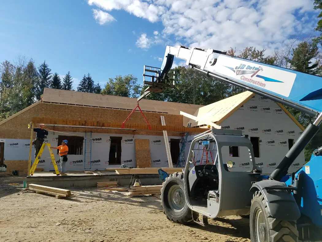 JB Cote Construction crew framing a new home with a telehandler lifting roof trusses into place