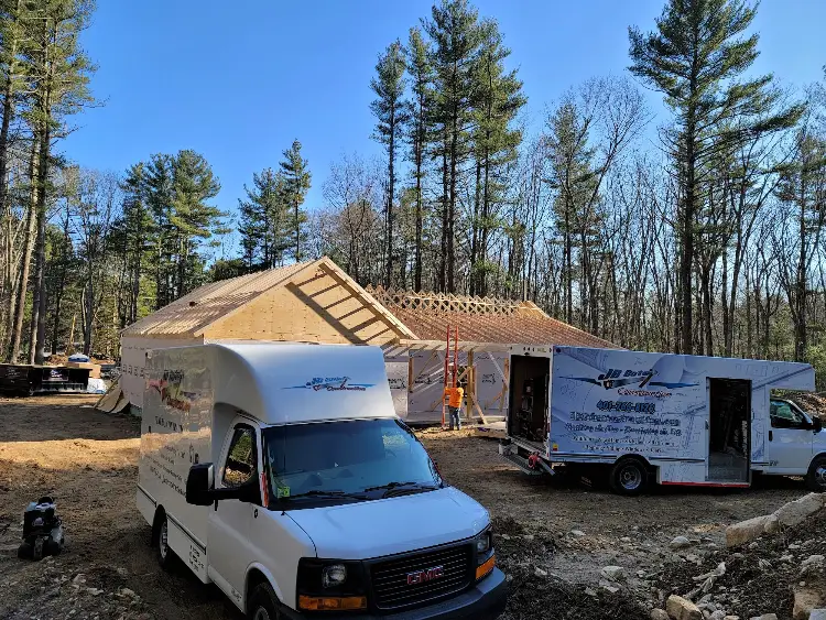 JB Cote Construction work vans parked at a wooded job site while a new home is framed