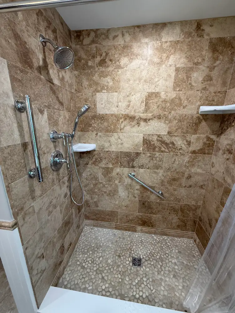 Tiled walk-in shower with grab bars, a handheld shower head, and a pebble stone floor built by JB Cote Construction