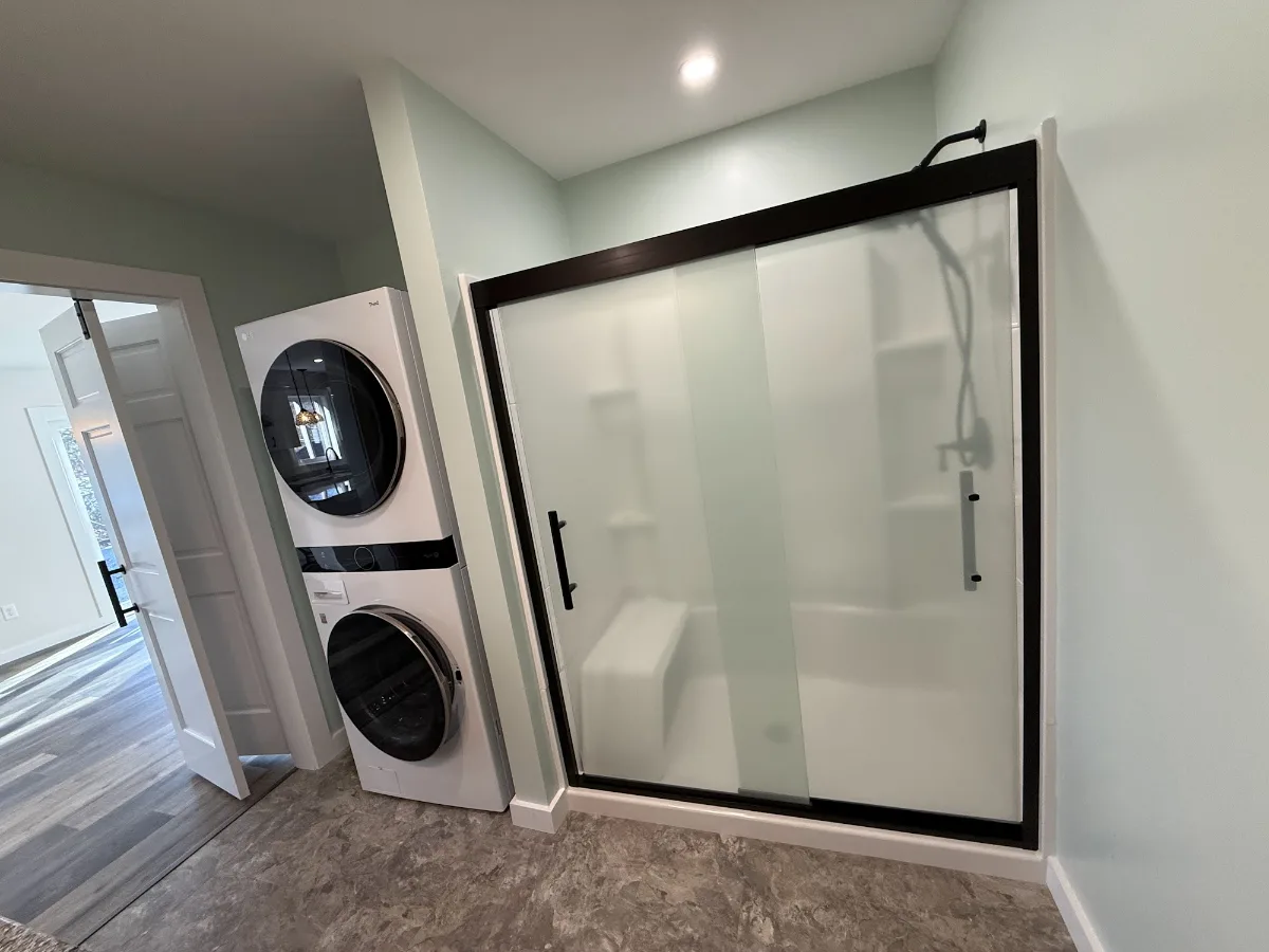 Bathroom with a walk-in shower behind a sliding glass door and a stacked washer and dryer, built by JB Cote Construction